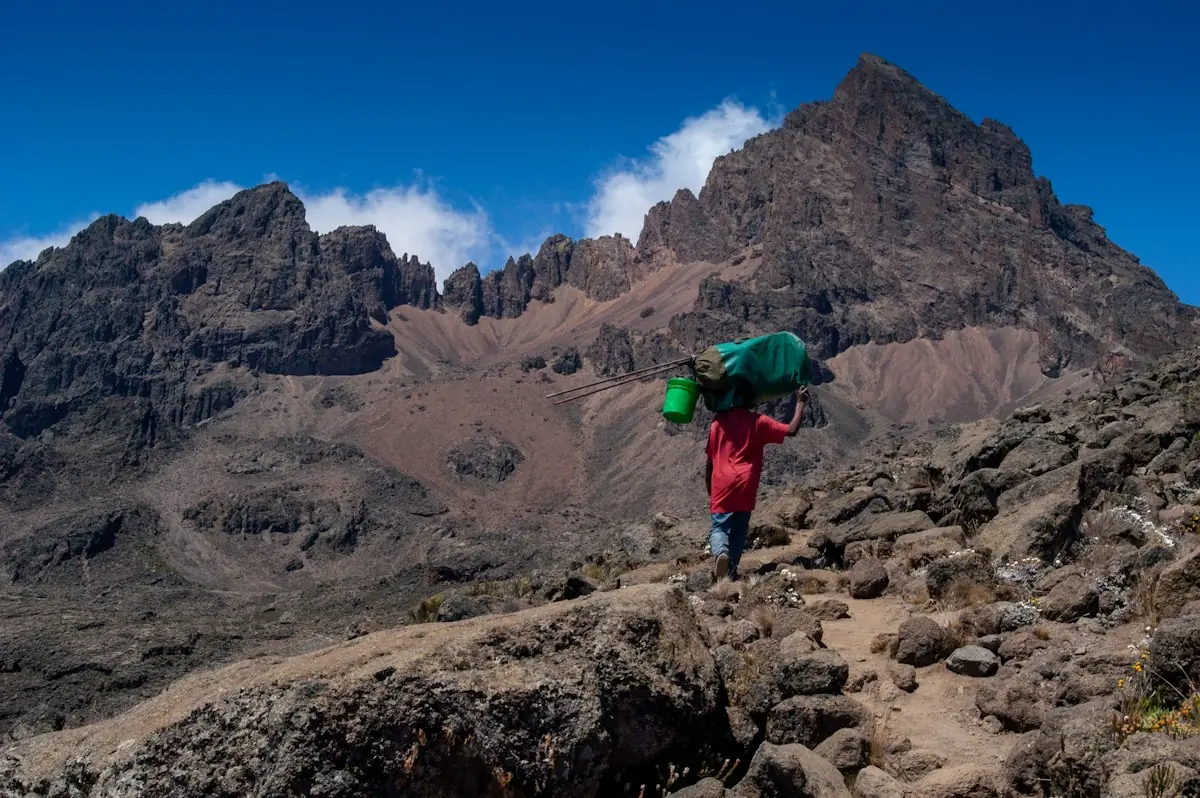 A porter carrying a heavy load up a rocky mountain trail