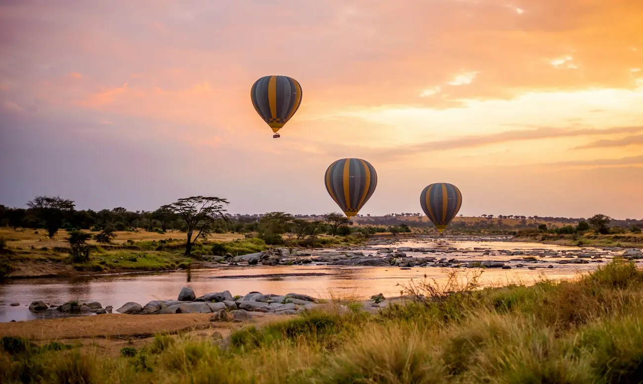 Hot-air balloons drifting over a river on the plains at sunset